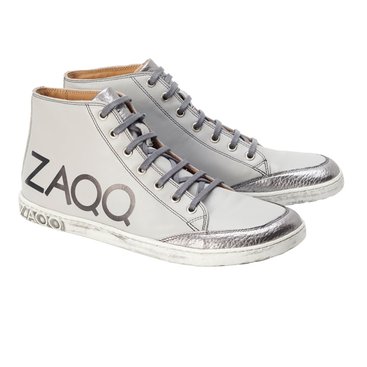 Entdecken Sie die ideale Kombination aus Stil und Komfort mit den SQYLA Grey High-Top-Sneakern von ZAQQ. Diese Sneaker sind mit silbernen Metallic-Akzenten und Markendetails verziert und aus hochwertigem Nappaleder gefertigt. Sie verfügen über ein klassisches Schnürdesign gepaart mit einer weißen Kautschuksohle, die für einen dezenten Used-Look sorgt.