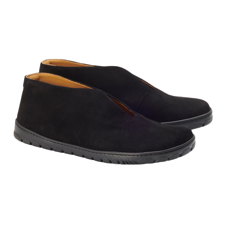 Ein Paar TSEQA Black-Schuhe von ZAQQ aus Wildleder mit flacher OUTDOOR-Sohle, aufgenommen von der Seite und etwas von oben. Diese Slipper zeichnen sich durch ein schlichtes und minimalistisches Design aus, wobei an den Rändern eine hellbraune Innenseite sichtbar ist.