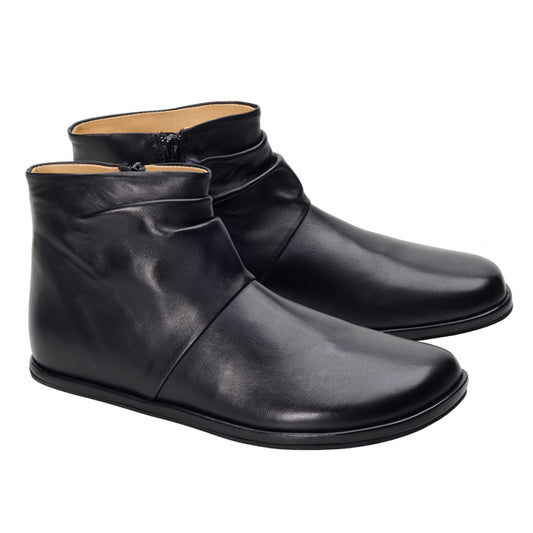 Wir präsentieren die schwarzen Stiefeletten QOURTNEY von ZAQQ: ein stilvolles Paar eleganter schwarzer Barfußstiefel aus Leder mit glatter Oberfläche und praktischen seitlichen Reißverschlüssen. Diese minimalistischen Stiefel zeichnen sich durch eine leicht abgerundete Spitze aus, die ihren makellosen weißen Hintergrund perfekt ergänzt und sowohl Stil als auch Komfort verkörpert.