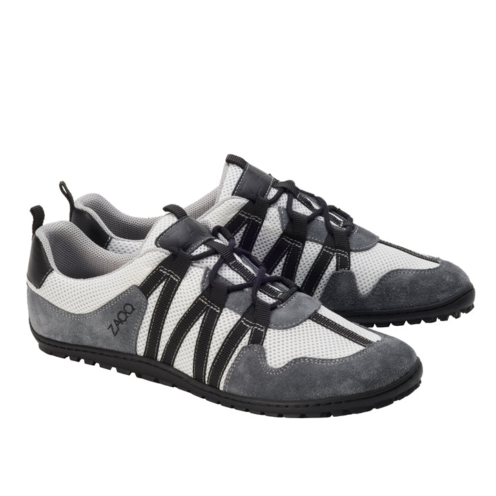 Wir präsentieren den RIQ Grey von ZAQQ, ein Paar stylische Sportschuhe mit einem eleganten grau-weißen Design mit schwarzen Akzenten und Schnürsenkeln. Dieser atmungsaktive Sneaker verfügt über ein strukturiertes Muster und eine robuste Sohle und eignet sich perfekt sowohl für die Freizeit als auch für sportliche Aktivitäten.