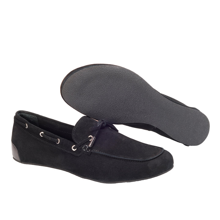 Wir präsentieren den FLIQ Black von ZAQQ, ein Paar schwarze Wildleder-Loafer im klassischen Mokassin-Design. Diese Schuhe sind aus hochwertigem Ziegenveloursleder gefertigt und verfügen über ein Lederschnürdetail mit silbernen Ösen für außergewöhnlichen Komfort. Ein Schuh steht aufrecht, während der andere auf der Seite liegt, um die sichtbare Gummisohle zu präsentieren.