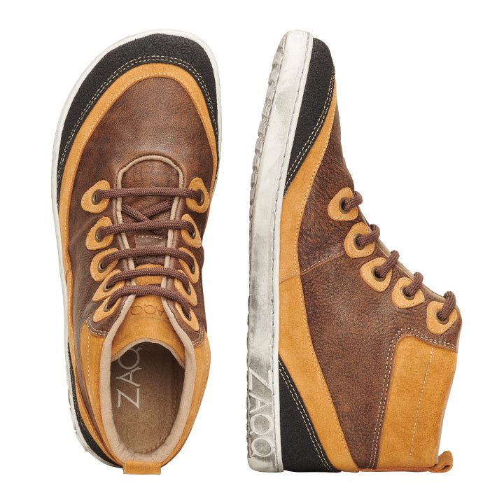 Zwei Paare CINQO Brown von ZAQQ zeichnen sich durch orange und schwarze Akzente aus. Ein Schuh ist von oben abgebildet und betont seinen Schnürstil, während der andere das ZAQQ-Branding auf der weißen Sohle für einen eleganten Barfußschuh-Look zeigt.