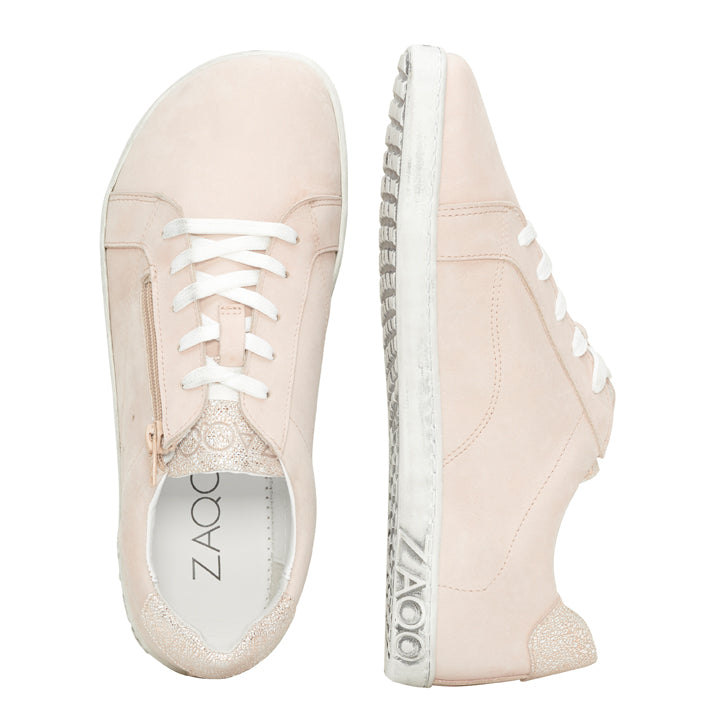 Ein Paar QOMFY Wide Rosa-Sneaker von ZAQQ in hellrosa Design mit weißen Schnürsenkeln und Sohlen. Ein Schuh ist von oben abgebildet und zeigt die Innensohle mit dem ZAQQ-Branding, während der andere von der Seite gezeigt wird, um die detaillierten Nähte und die Sohlenstruktur aus hochwertigem Nappaleder hervorzuheben.