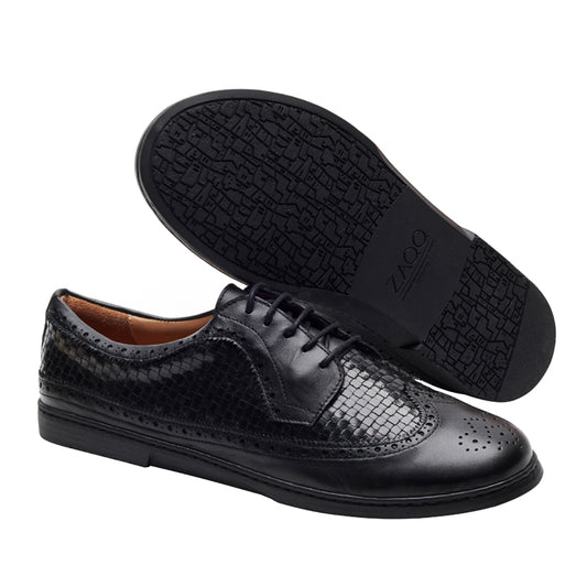 Ein Paar glänzende ZAQQ BRIQ Brogue Tresse Black Abendschuhe mit strukturiertem Muster an den Seiten und Flügelkappen-Design an der Spitze. Ein Schuh liegt auf der Seite, wodurch die gemusterte Sohle hervorgehoben wird, während der andere aufrecht steht.