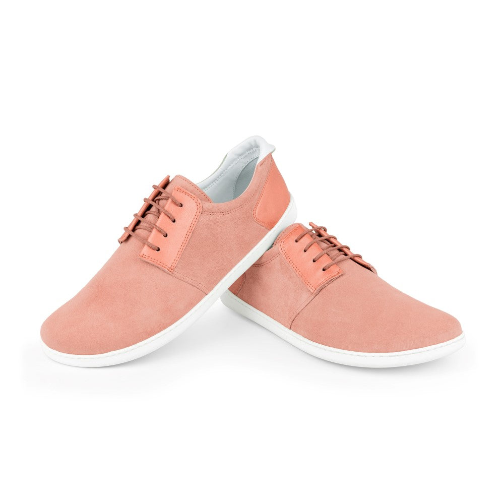 Ein Paar PIQUANT Rosa Schnürschuhe von ZAQQ mit rosa Veloursleder-Obermaterial und weißer Sohle wird vor einem schlichten weißen Hintergrund präsentiert. Ein Sneaker steht aufrecht, während der andere daran lehnt und sowohl die Draufsicht als auch die Seitenansicht zeigt.