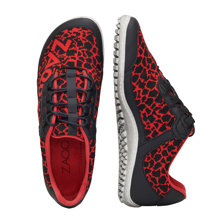 Die QASEY Red Sneaker von ZAQQ sind ein Paar stylische vegane Barfußschuhe in Rot, verziert mit einem schwarzen geometrischen Muster. Sie verfügen über flexible Gummisohlen, schwarze Schnürsenkel und ein einzigartiges Profildesign. Ein Sneaker ist von oben abgebildet, während der andere von der Seite gezeigt wird, um sein schlankes Design zu präsentieren.