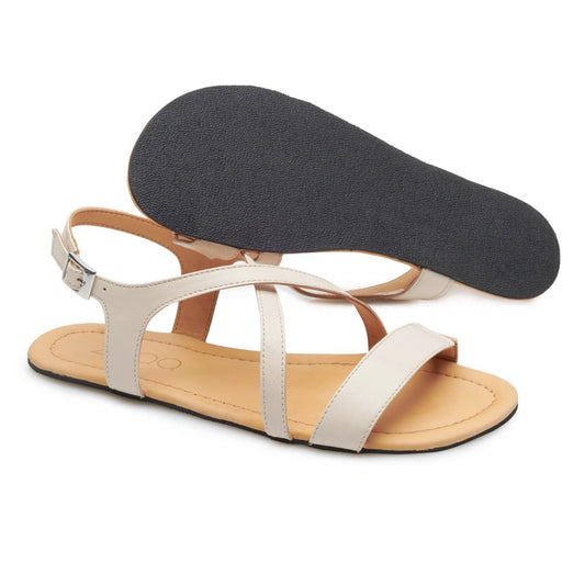 Die QEE Beige Sandalen von ZAQQ zeichnen sich durch ein beiges Riemchendesign mit offenen Zehen und verstellbaren Knöchelriemen aus, hervorgehoben durch eine flexible schwarze Kautschuksohle. Eine Sandale ist von der Seite zu sehen, während die andere ihre Sohle zeigt. Sie dienen als idealer femininer Sommerschuh für stilvollen Komfort.