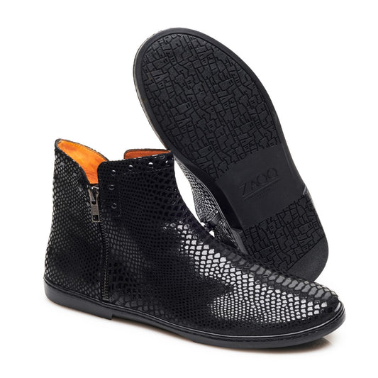 Wir präsentieren die QUAKERTOWN Black von ZAQQ, ein Paar eleganter Stiefeletten aus Nappaleder. Diese Stiefel haben ein schickes Strukturmuster, seitliche Reißverschlüsse und sind mit einem leuchtend orangefarbenen Innenfutter akzentuiert. Ein Stiefel steht vertikal, um die bequeme Passform hervorzuheben, während der andere angewinkelt ist, um das einzigartige geometrische Design der Sohle zu zeigen.