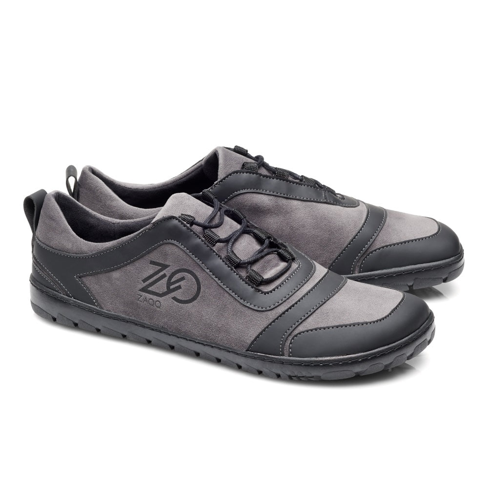 Die SQILL Ash Schuhe von ZAQQ sind ein Paar grau-schwarze Freizeitschuhe mit Schnürsenkeln, die das Logo der Marke an der Seite zeigen. Diese veganen Laufschuhe bieten ein schlankes Design mit einer robusten Sohle und sind somit perfekt für den Alltag oder Outdoor-Abenteuer.