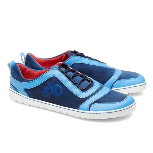 Wir präsentieren den SQILL Ocean von ZAQQ: Diese schicken blauen Sportschuhe präsentieren eine Mischung aus Wildleder- und Ledertexturen, gepaart mit weißen Sohlen, rotem Innenleben und dunkelblauen Schnürsenkeln. Das ZAQQ-Logo ist prominent an der Seite angebracht. Als veganer Barfußschuh bieten sie superleichten Komfort mit 2 mm Langzeitdämpfung für anhaltenden Halt.