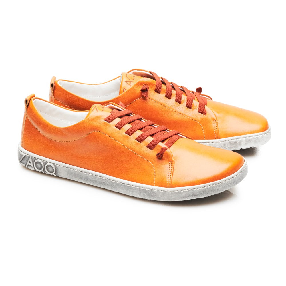 Ein Paar leuchtend orangefarbene STIQ Sierra-Sneaker mit weißer Sohle und orangefarbenen Schnürsenkeln. Die Schuhe, die an der Ferse mit der Marke ZAQQ versehen sind, sind schräg positioniert, um ihr schlankes Design und ihre auffällige Farbe hervorzuheben.