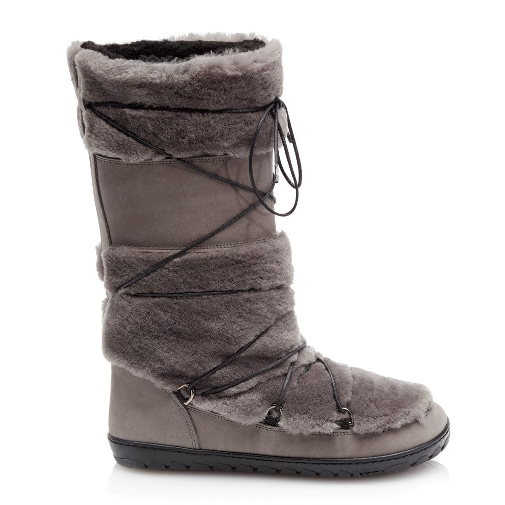 Eine Seitenansicht des TORQ Winterstiefels von ZAQQ zeigt sein hohes Design mit grauem Wildleder und Fell, ähnlich einem eleganten Fellstiefel. Er verfügt über schwarze, überkreuzte Schnürsenkel und eine robuste Sohle. Die weiche und plüschige Außenseite des Stiefels bietet sowohl Stil als auch Wärme.