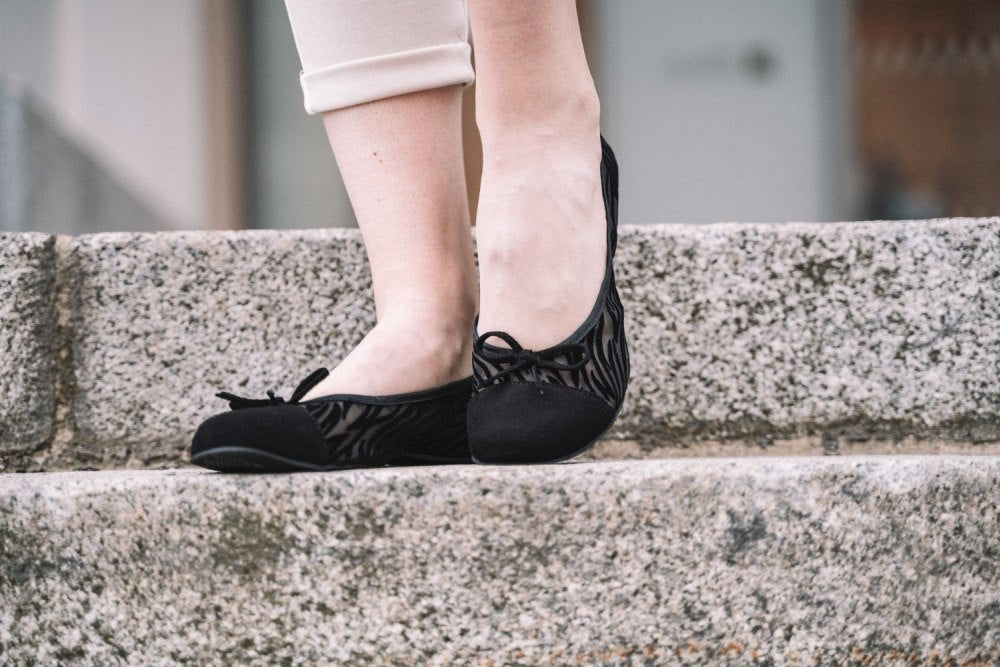 Eine Person in den TWIST Sling Black Ballerinas von ZAQQ mit flexibler Sohle steht auf Steinstufen. Nur Beine und Füße sind zu sehen.