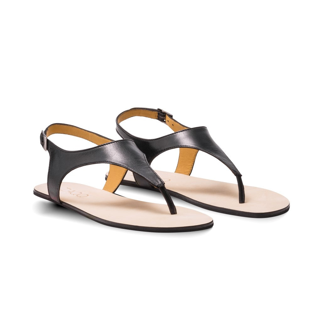 Wir präsentieren die QAVA Black von ZAQQ: Ein Paar schicke Zehentrenner-Sandalen mit Knöchelriemen und flacher beiger Sohle, alles sorgfältig aus hochwertigem Nappaleder gefertigt. Diese minimalistischen Sandalen sind die perfekte Ergänzung zu Casual-Outfits und kommen auf weißem Hintergrund wunderschön zur Geltung.