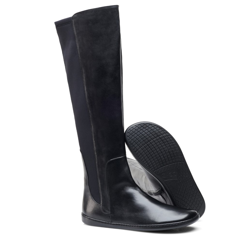 Ein Paar elegante, schwarze, kniehohe Lederstiefel mit niedrigem Absatz von ZAQQ in QATCH Nappa Black. Ein Stiefel steht aufrecht, während der andere zur Seite geneigt ist und seine strukturierte Gummisohle zur Schau stellt.