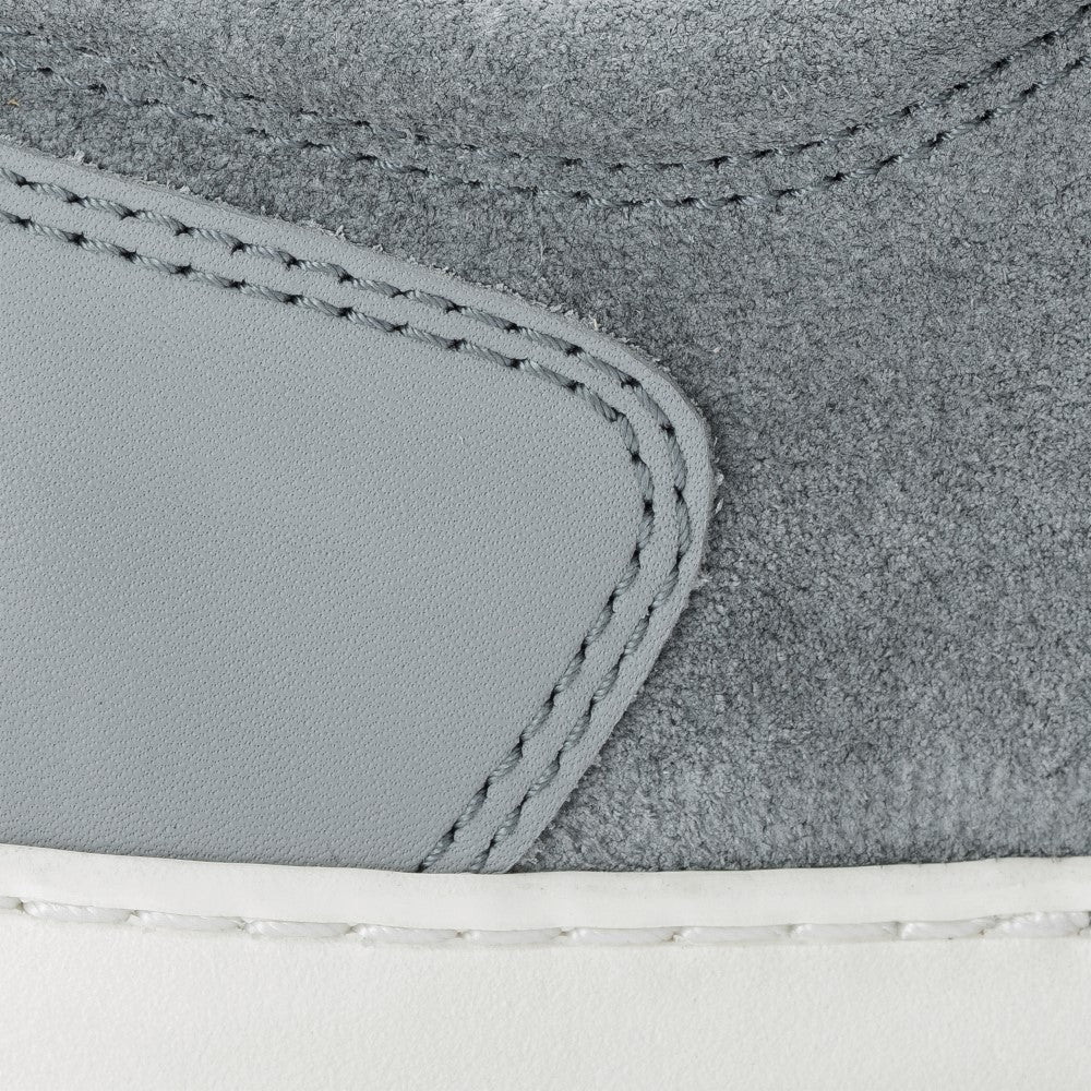 Diese Nahaufnahme des ZAQQ PIQUANT Grey Sneakers zeigt sein graues strukturiertes Wildleder und graue Ledereinsätze. Das Design wird durch sichtbare Nähte akzentuiert, während ein Blick auf die weiße, flexible Sohle Komfort bei jedem Schritt suggeriert.