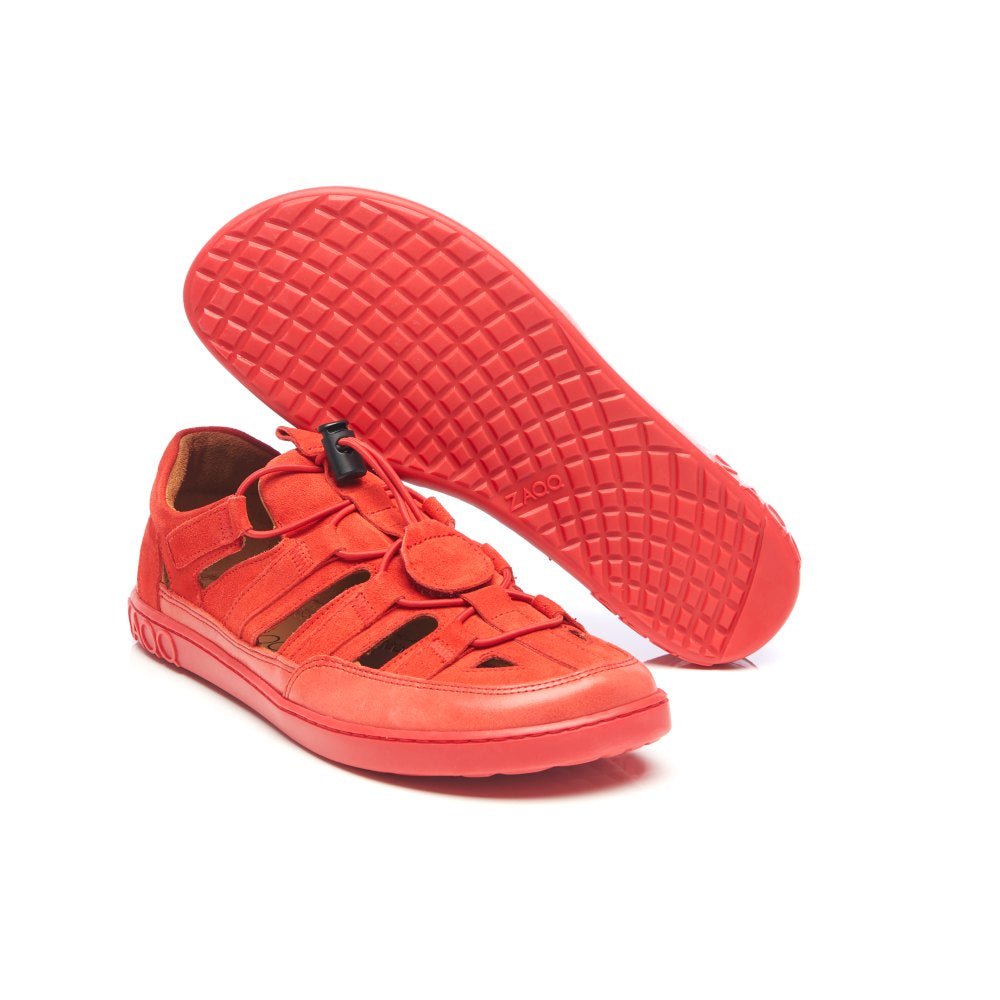 Wir präsentieren den QLEAR Red von ZAQQ, ein lebhaftes Paar Freizeitschuhe in leuchtenden Orangetönen mit auffälligen schwarzen Akzenten, perfekt als Sommer-Outdoorschuh. Ein Schuh steht aufrecht, während der andere seine aufwendig strukturierte Sohle zur Schau stellt. Dieses moderne Design umfasst sowohl einen Knebel- als auch einen Klettverschluss und ist damit die ideale Wahl für Abenteuerlustige.