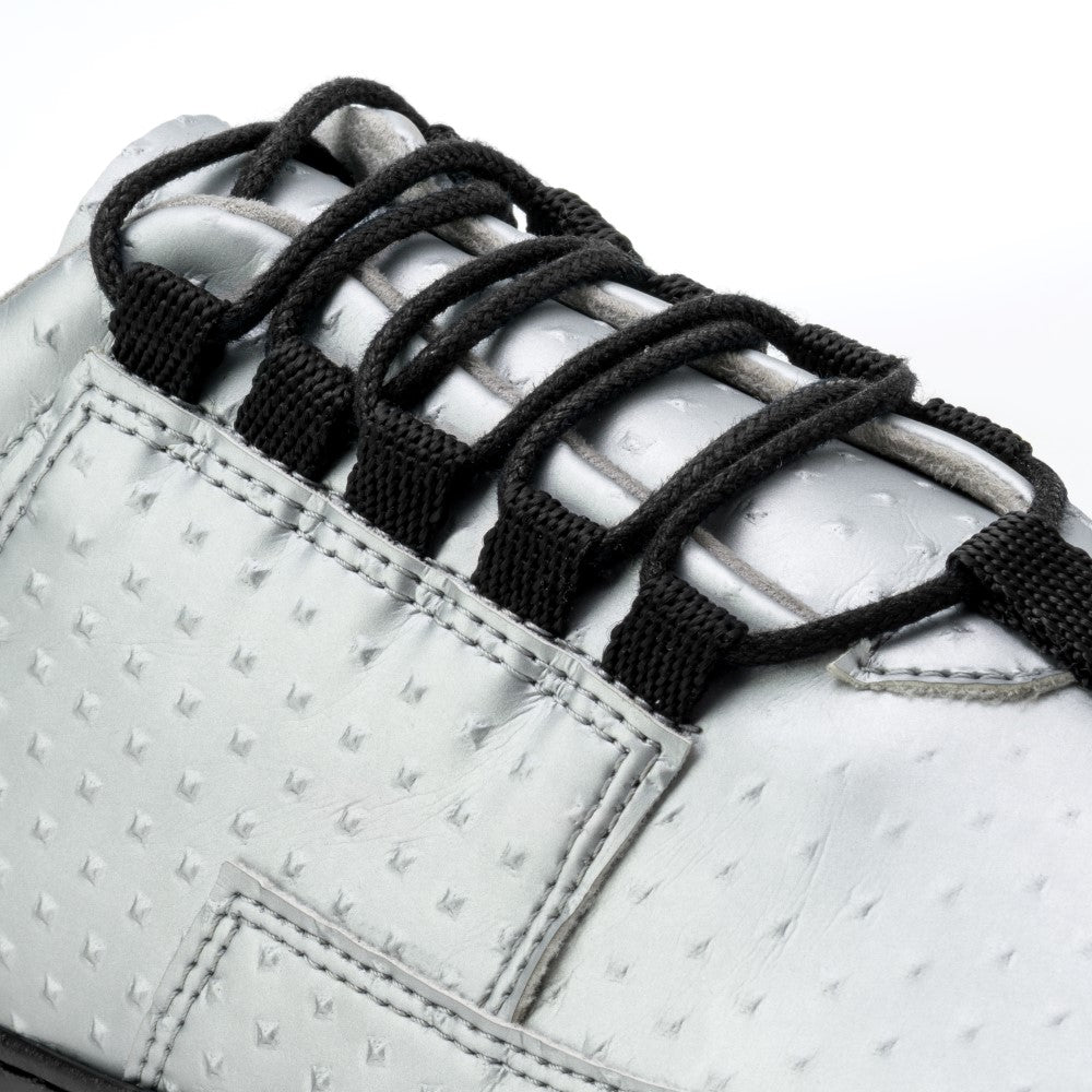 Nahaufnahme des JAQ Silver Barfuß-Sneakers von ZAQQ mit strukturiertem Punktmuster und schwarzen Schnürsenkeln. Dieser ultraleichte Schuh verfügt über mehrere Schnürsenkelschlaufen und eine flexible Gummisohle vor einem schlichten Hintergrund.